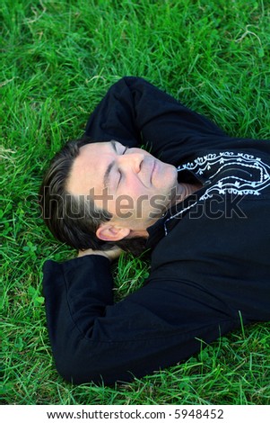 Man lying on the grass in a zen position with eyes closed, resting.