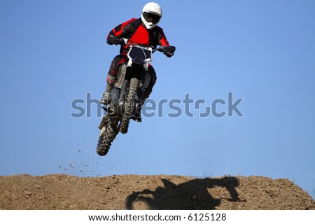 Man jumping high in a motocross bike across a slope on a desert.
