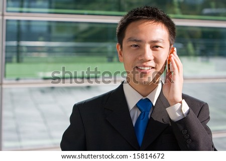 Good looking asian business man standing with formal suit and mobile phone.