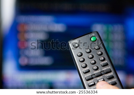 Hand holding a remote control pointing to a blurred TV program