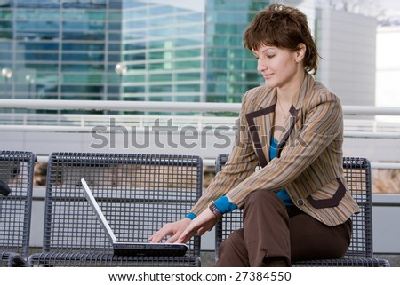 Beautiful young brunette woman using a computer laptop outdoors in front of an office building