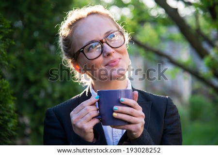 Girl in glasses holding a blue cup in hands. Girl smiles and looks into the distance.