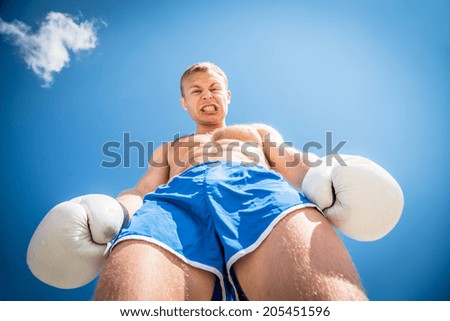 Athletic guy in blue shorts, boxing gloves against a blue sky