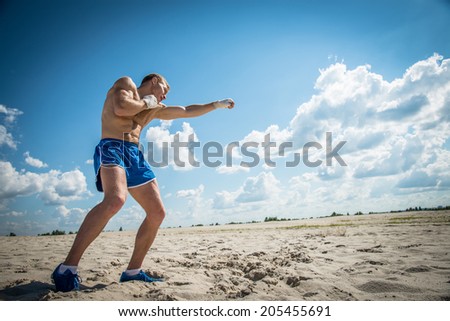 Athletic guy in blue shorts and boxing bandages fulfills kick exercising in nature