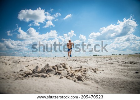 Athletic guy in blue shorts and sunglasses running along the golden sand and blue sky
