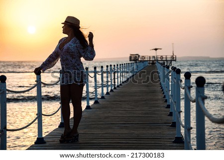 Silhouette of a girl standing on the pier, in the beautiful blue sea during the dawn of the sun
