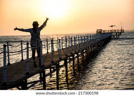Silhouette of a girl standing on the pier, in the beautiful blue sea during the dawn of the sun