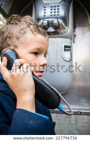 Child dials a phone number in a phone booth