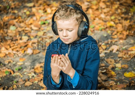 Boy playing in the game in touchscreen phones, while listening to music with big headphones