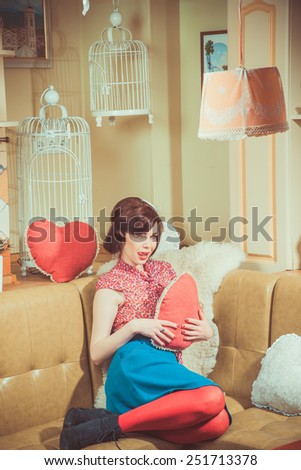 Young girl in red stockings sits on a couch and holding a big red heart