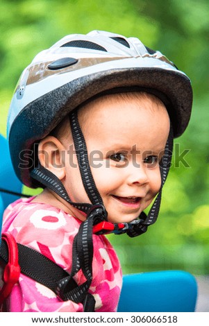 Little girl dressed in bicycle helmet and sits on a bicycle seat for children. \
\
Emotion: smile