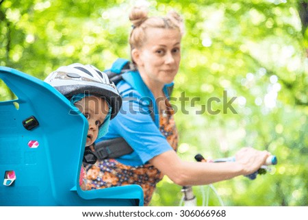 Mom on a bike with a small child, who wore a bicycle helmet and sitting on a bicycle seat for small children