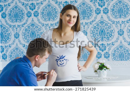 happy man draws on his belly pregnant wife