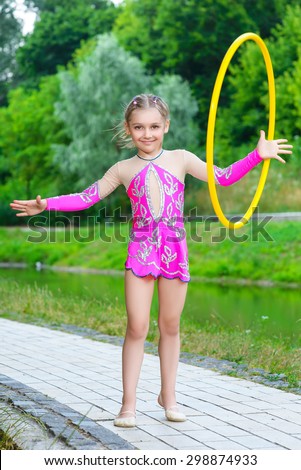 fitness, sport, people and healthcare concept - little sporty girl exercising with hula hoop over park background