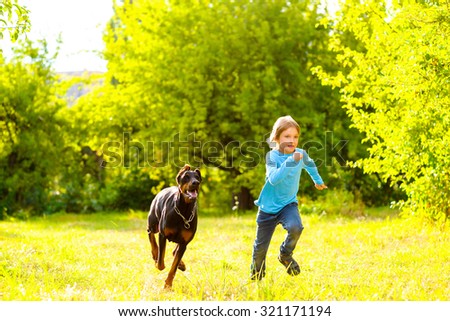 boy running away from dog or doberman in summer park