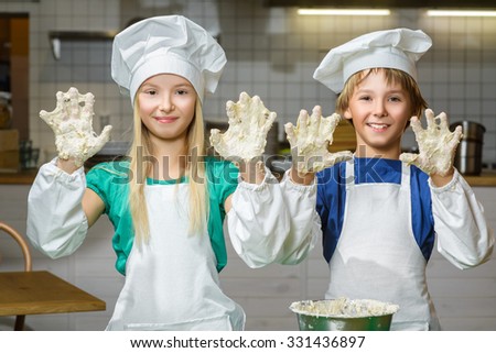 Funny happy chef boy width girl cooking at restaurant kitchen and knead the dough in a bowl