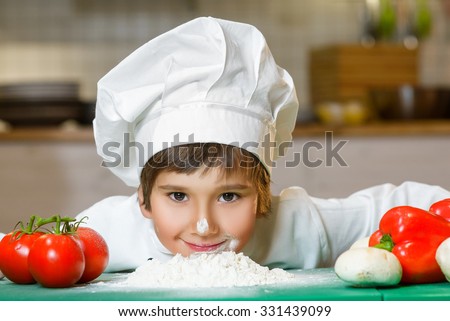 Funny happy chef boy cooking at restaurant kitchen and bent over the flour