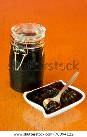 Glass jar and white bowl of blackberry jelly on old, wooden table