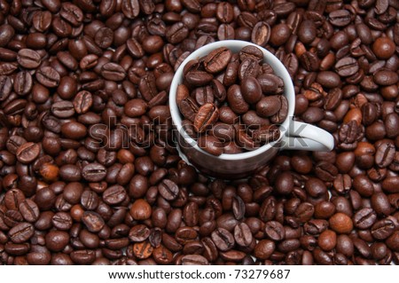 Overhead shot of a cup filled with roasted coffeee beans surrounded by more roasted beans