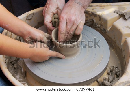Potters hands guiding a child hands to help him to work with the ceramic wheel