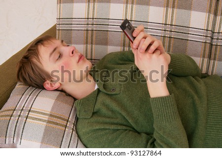 Young man lying down on the sofa, sending text message on mobile phone.