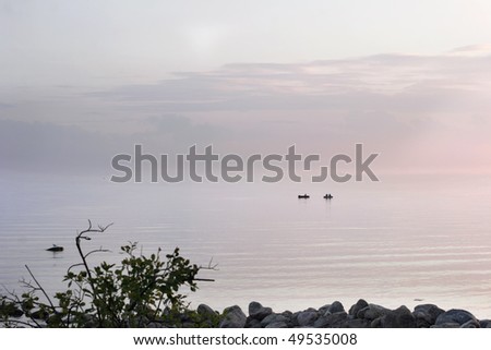 Sea landscape at sunset with fishermen and little fog above water