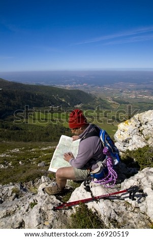 Orienteering - A trekker consulting a map, alone on a mountain, over a clear blue sky