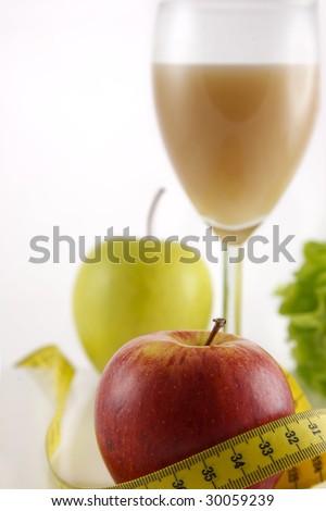 A natural juice glass surrounded by a set of fruit and vegetables, framed by a measuring tape