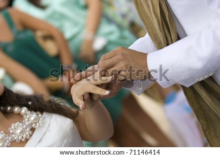 The groom places the wedding ring on the bride\'s hand, over blurred background