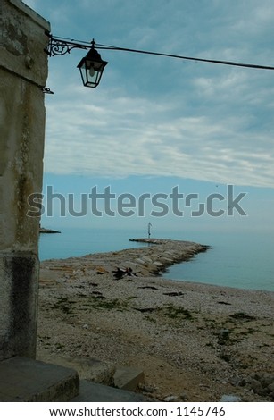 A family eats lunch on a cloudy day near a stone port on Adriatic beach in southern Italy
