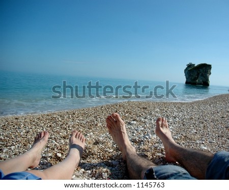 A couple enjoys the sun on an isolated private beach in Southern italy as the look past their feet at the Adriatic sea