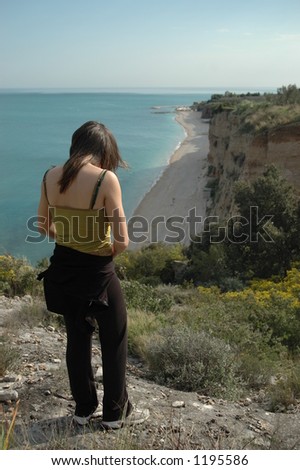 Young attractive female stands on a cliff relaxing a enjoying her view of the Adriatic Sea and Fontana de la Rosa from Gargano National Park in Southern Italy