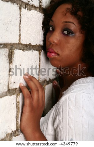 african american girl with innocent look showing blank expression leaning her face to white brick wall