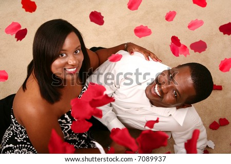 african american couple holding each other looking up to the camera with falling rose petal