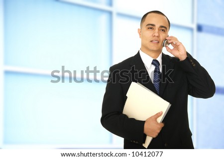 business man holding folder and making a phone call on his way out of office hallway