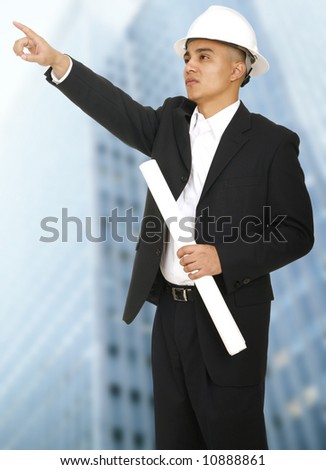 a man wearing hard hat in business suit pointing at something with tall building behind him