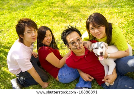 a group of four asian teens laying back on grass holding a white puppy labrador