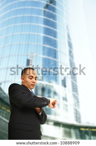 business man looking at his watch with tall business building behind him