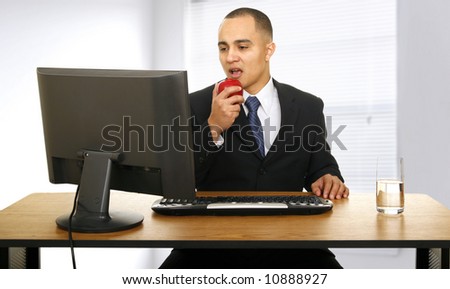 an office worker eating apple in his office and looking at computer screen