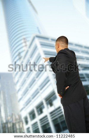 a man pointing at tall business building in downtown area with other hand on his hip