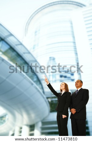 business people standing in front of modern building. the woman pointing up to somewhere. concept for success or business plan