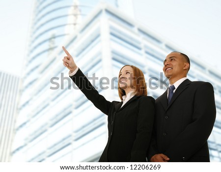 two business people, man and woman standing in front of business building. the woman pointing to somewhere. concept for business team or business plan