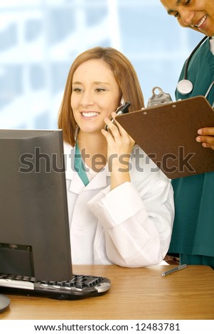 doctor calling on the phone and looking at her computer while her assistant on her back holding clip board. medical concept in modern office
