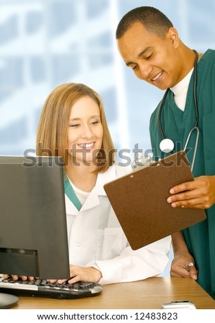 two medical people looking at same clip board and smiling. the woman is sitting down and the nurse is standing