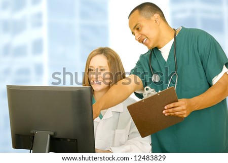 nurse in medical uniform pointing at computer screen with his assistant sitting down. both showing happy expression. concept for team work