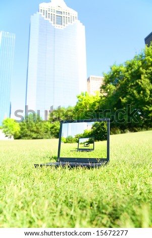 a computer sits on the grass with downtown building on the background. computer screen showing repeated pattern of the picture. concept for business, computer or technology