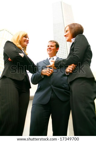 three business people discuss as a team outdoor with tall downtown building on the background