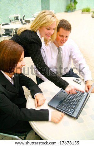 blond business woman pointing laptop to two of her associates. taken outdoor in cafe settings area