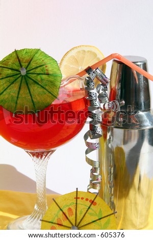 Cocktail shaker and red cocktail in tall glass with umbrella