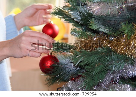 Hands hanging red baubles on christmas tree